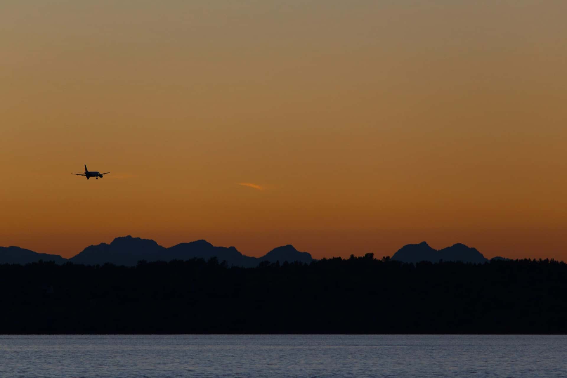 An aircraft in silhouette on its final approach against an amber sunset sky.
