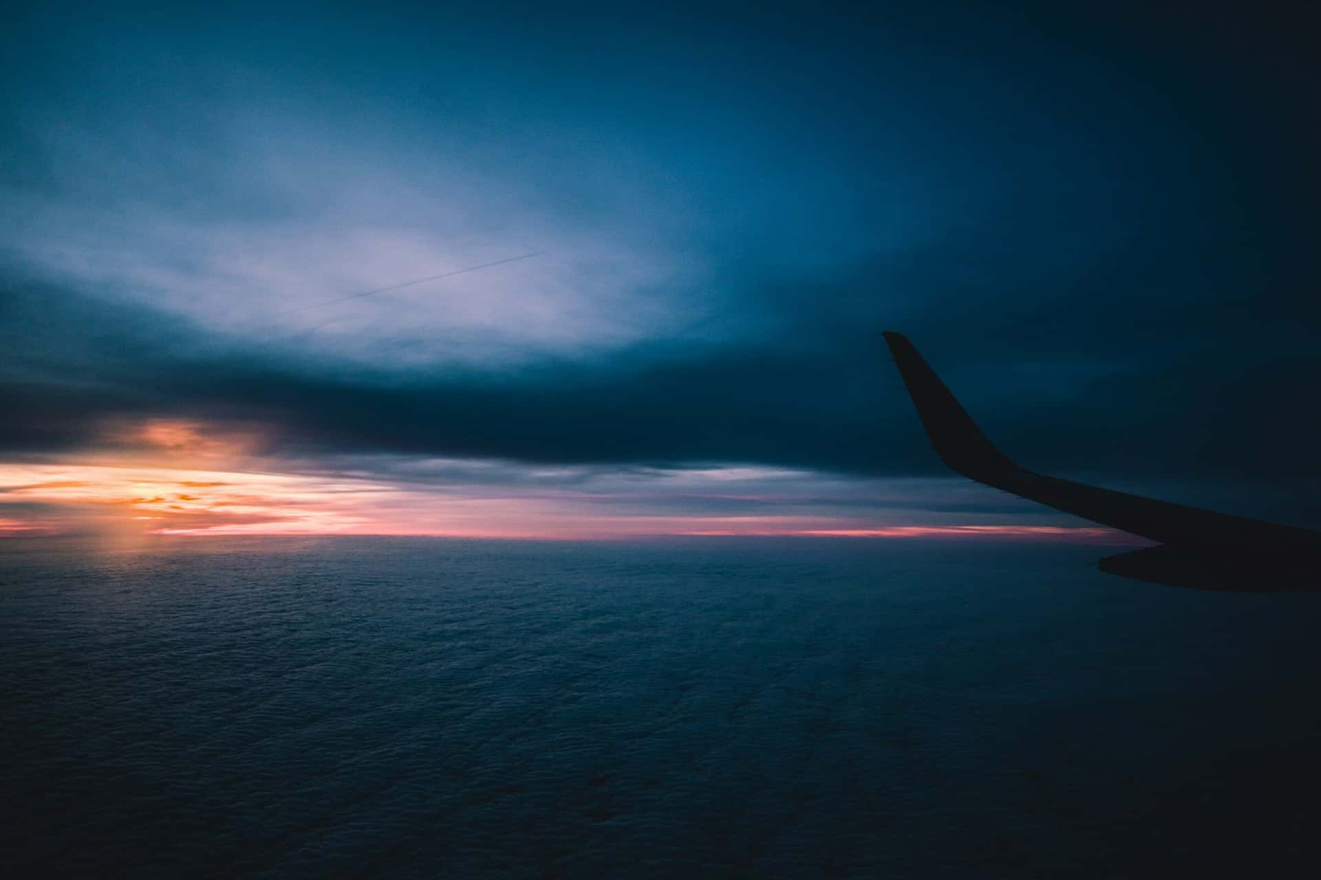 The wing of an aircraft in silhouette above the clouds as the sun sets.