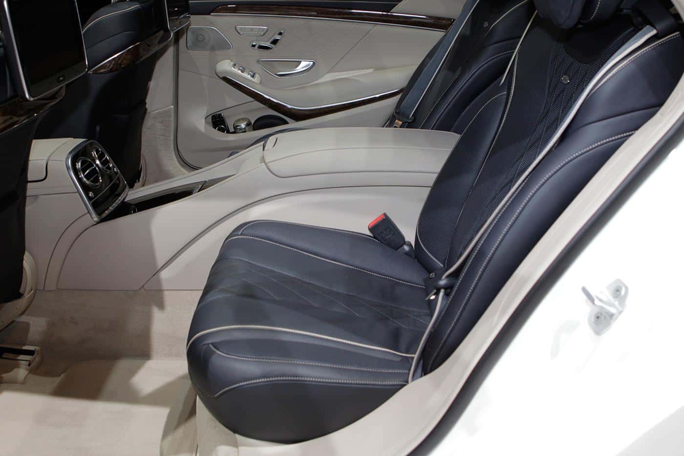 The back seat of a full-size Mercedes saloon: a navy quilted-leather bench with cream piping, cream leather and walnut door trim, and a chrome seat-control panel set into the door.