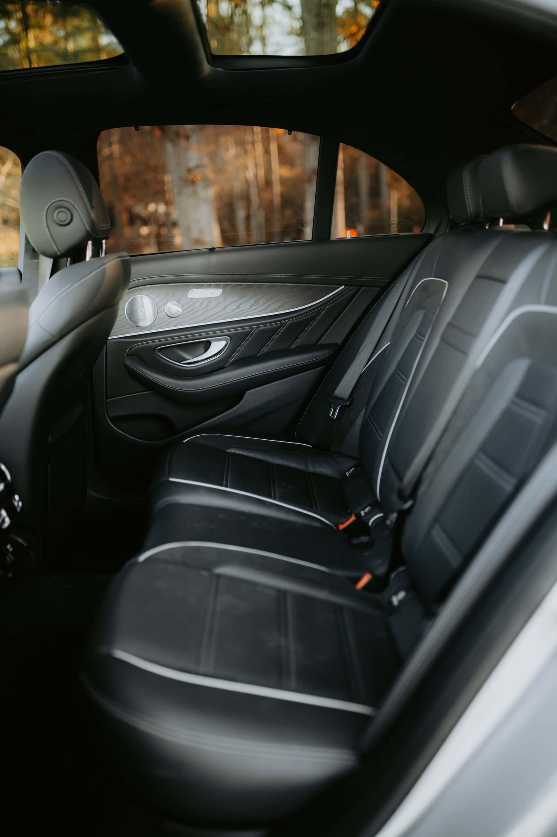 The rear seats of an executive saloon in black leather with white piping, the near-side door open on autumn woodland.