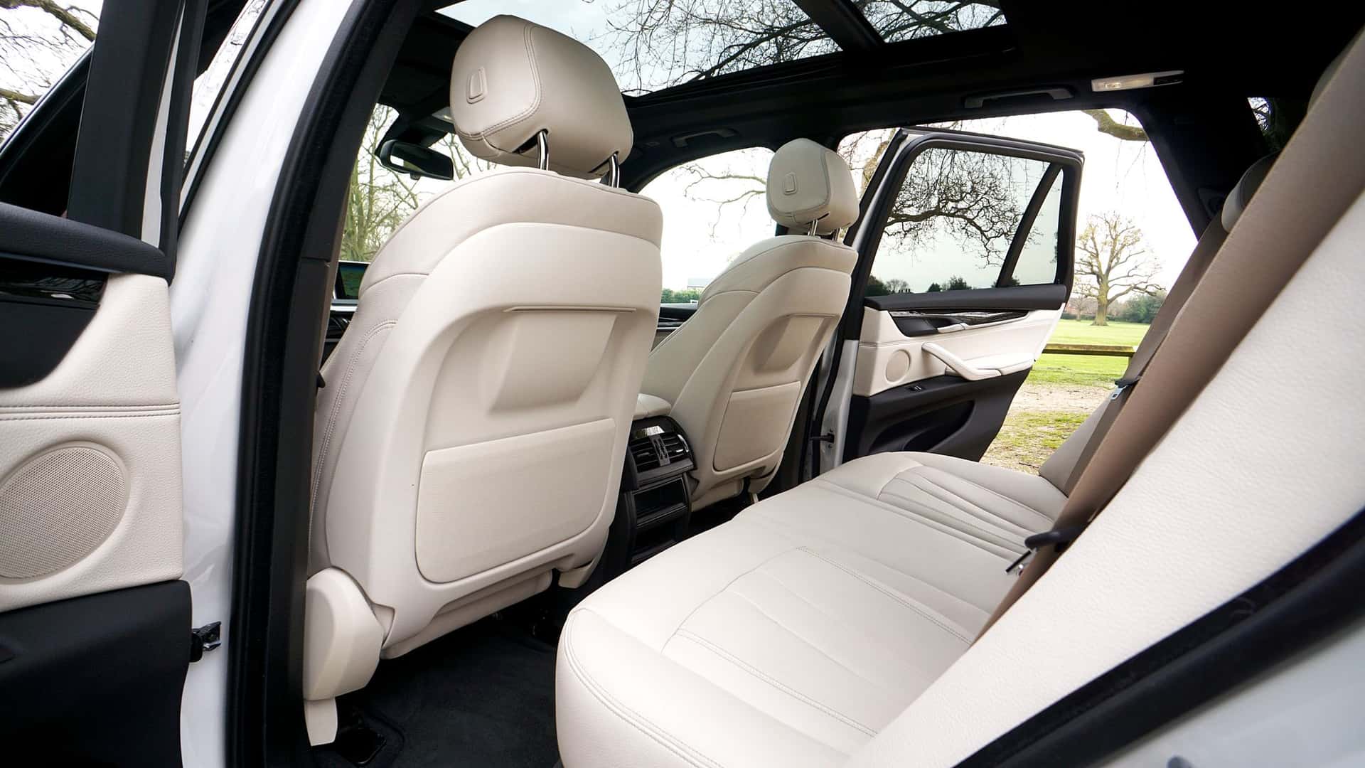 The rear cabin of a large estate car in ivory leather, both doors open on parkland and bare winter trees, the roof open to the sky.