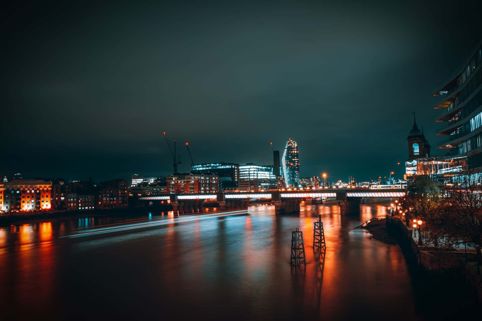 The Thames at night, with the lit City reflected in the water under Cannon Street railway bridge.